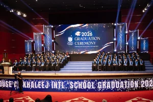 Wide shot of graduates seated on tiered stage steps beneath the "Class of 2026 Graduation Ceremony" screen display and professional beam lighting setup executed by Topaz Event Management.